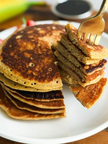 Fork taking a bite of a stack of banana oat flour pancakes.